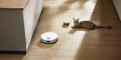 Biały robot odkurzający Xiaomi sprząta podłogę, a obok leży kot.