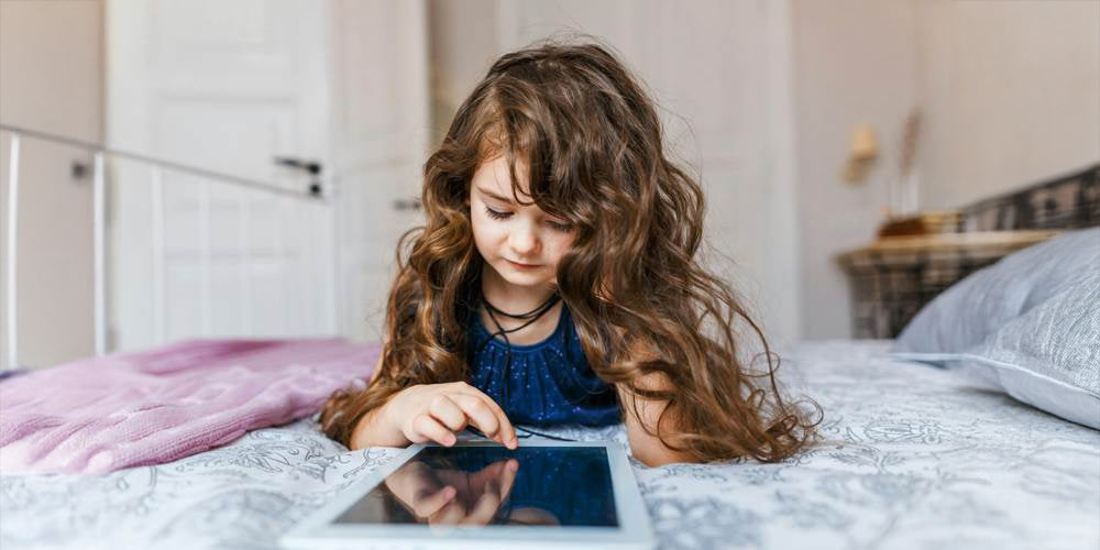 Dziewczynka przeglądająca tablet na łóżku w pokoju