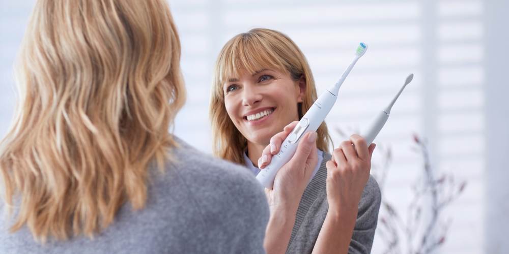 Kobieta o blond włosach myjąca zęby szczoteczką soniczną